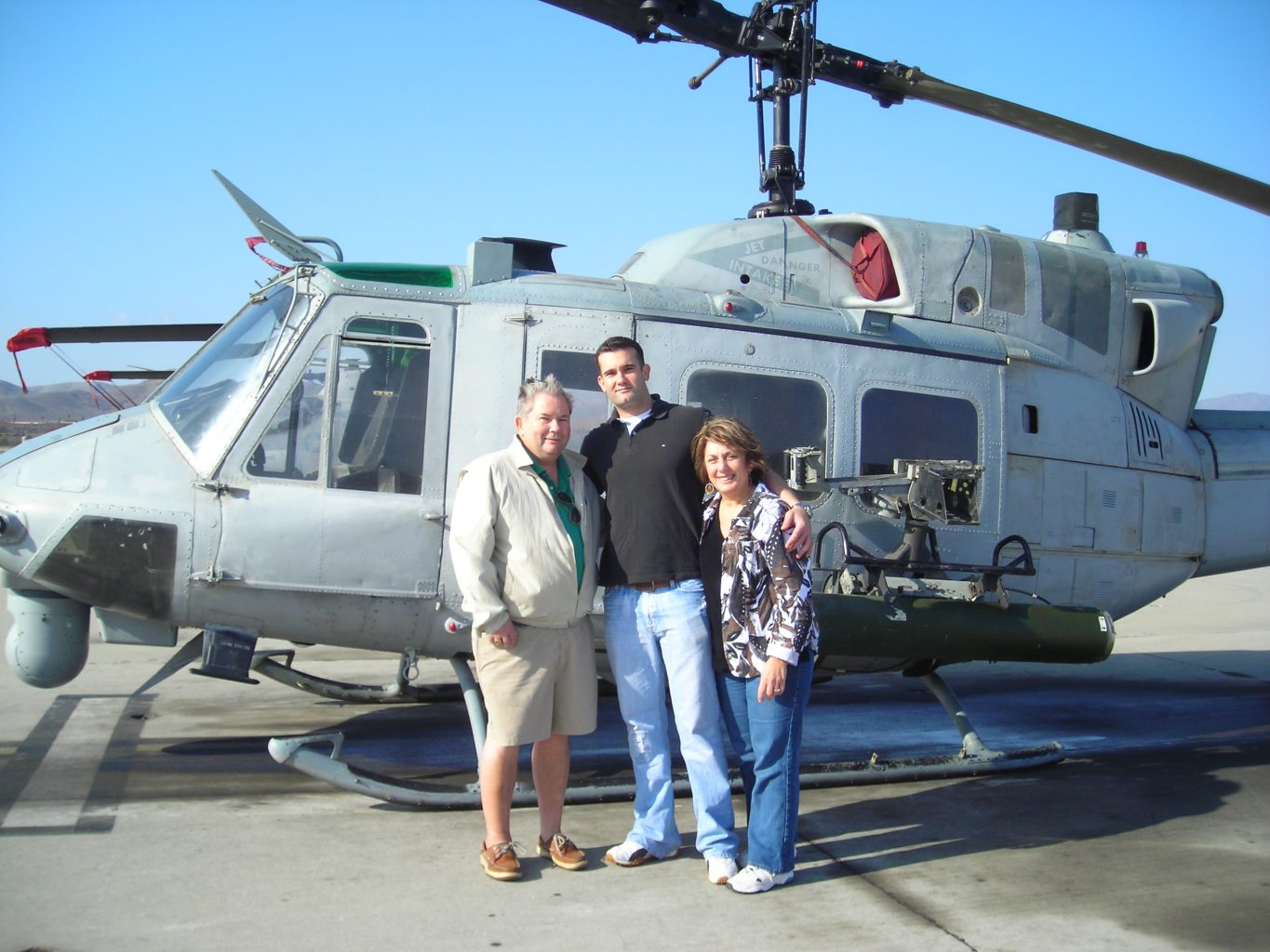 Photo of Captain Eric Jones (middle) with his father Ken (left) and mother Cyndy (right) in front of a Huey Helicopter.